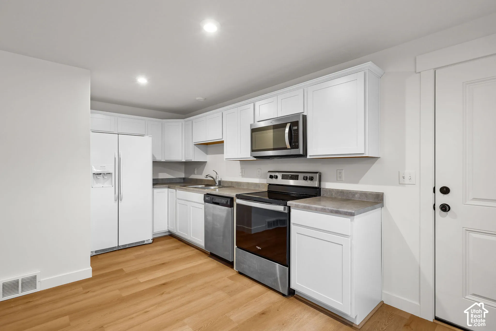Kitchen featuring white shaker-style cabinetry, stainless steel appliances, neutral stone-finish countertops, and wood-finish flooring