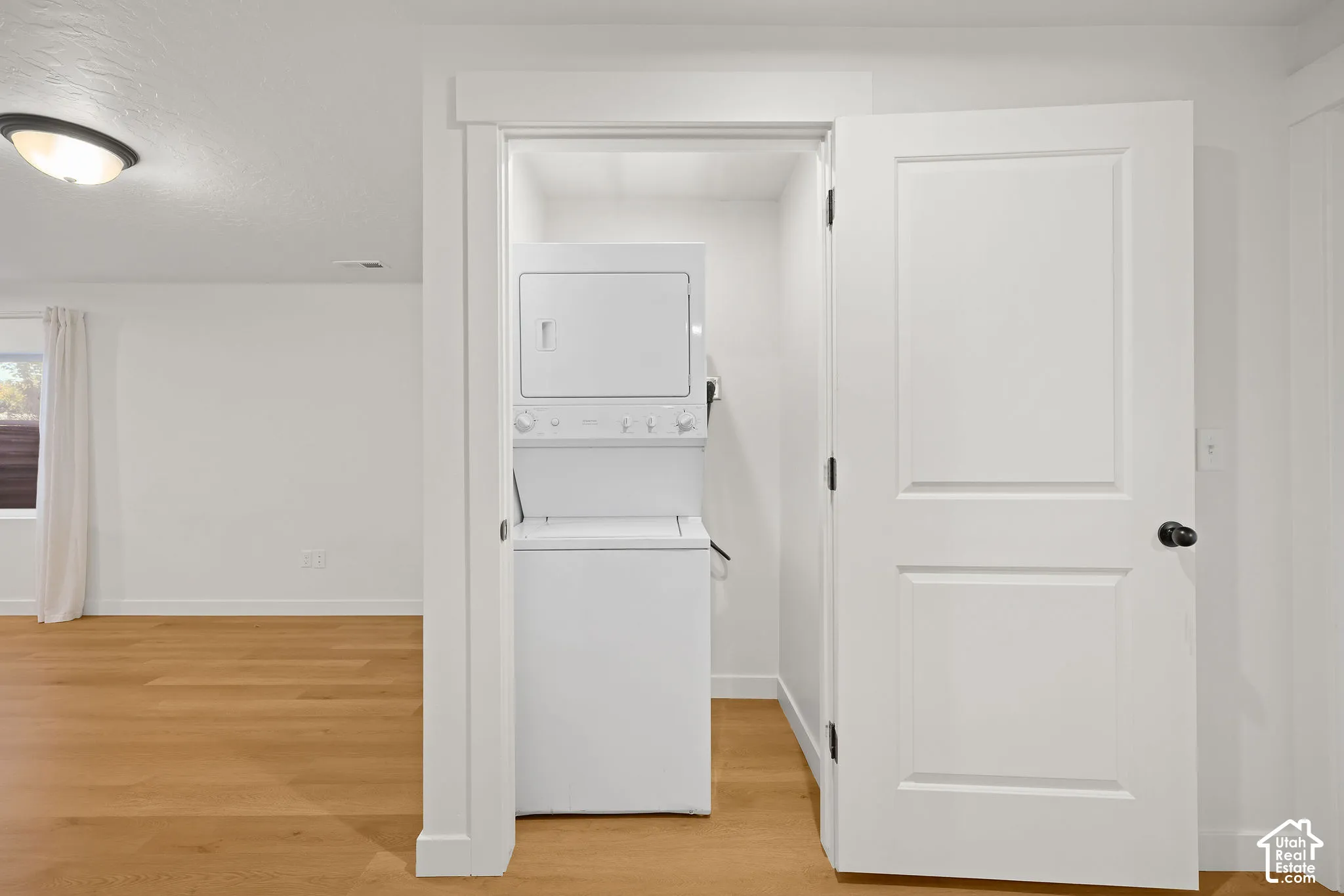 Dedicated laundry closet featuring a stackable washer and dryer, wood-finish flooring, and white interior trim