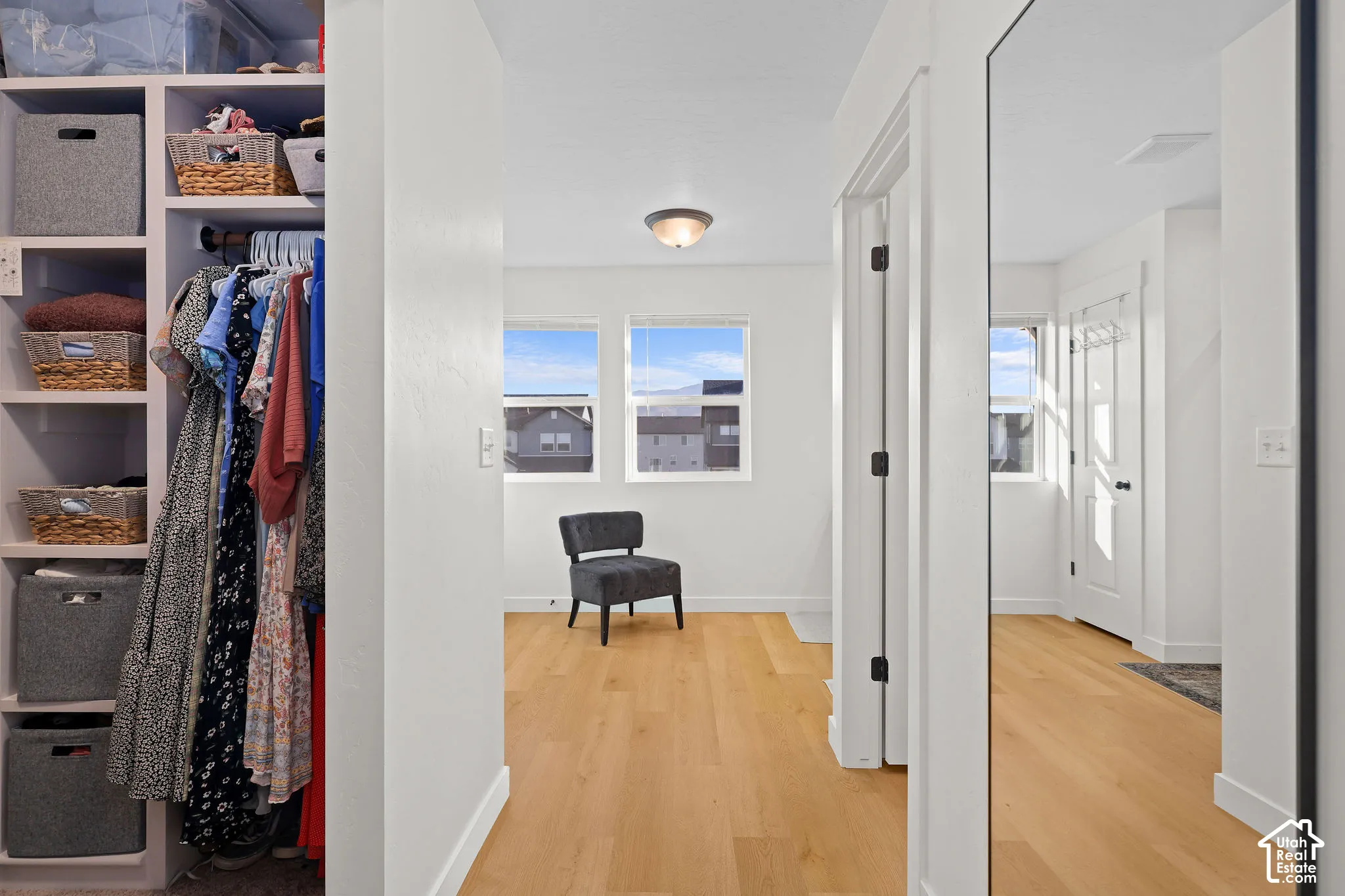 Custom built-in shelving with integrated hanging storage, wood-finish flooring, full-length wall mirror, and neutral wall tones