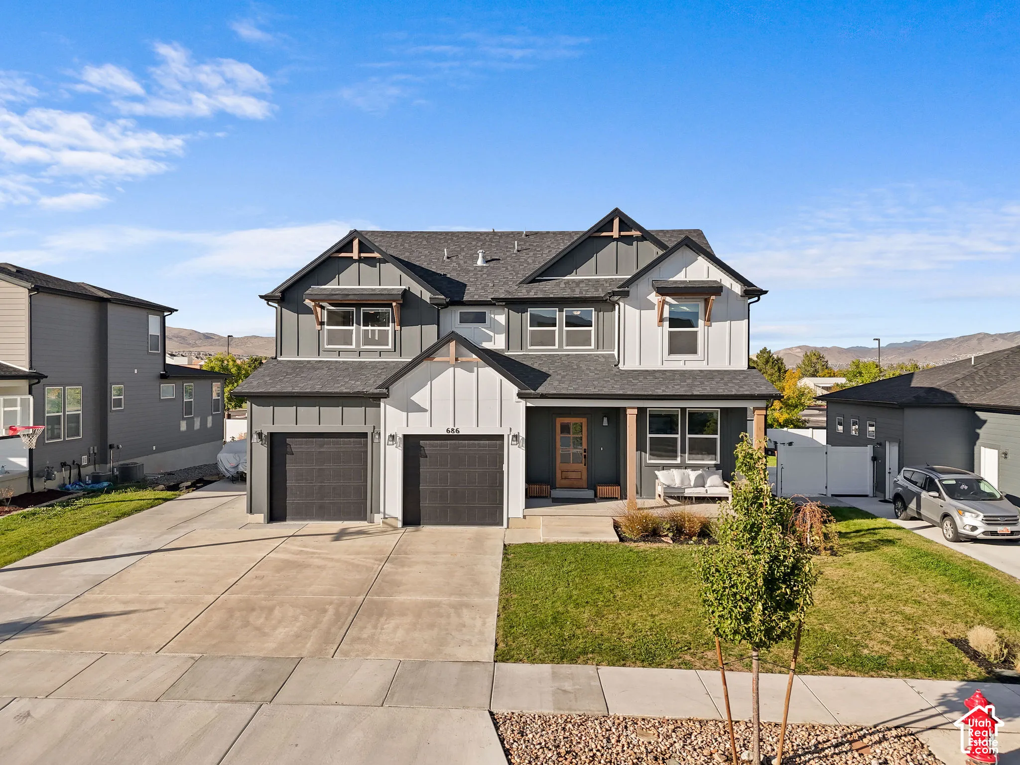 Two-story exterior featuring board-and-batten siding, a covered front entryway with timber posts, multiple roof gables, and a concrete driveway leading to a two-car garage