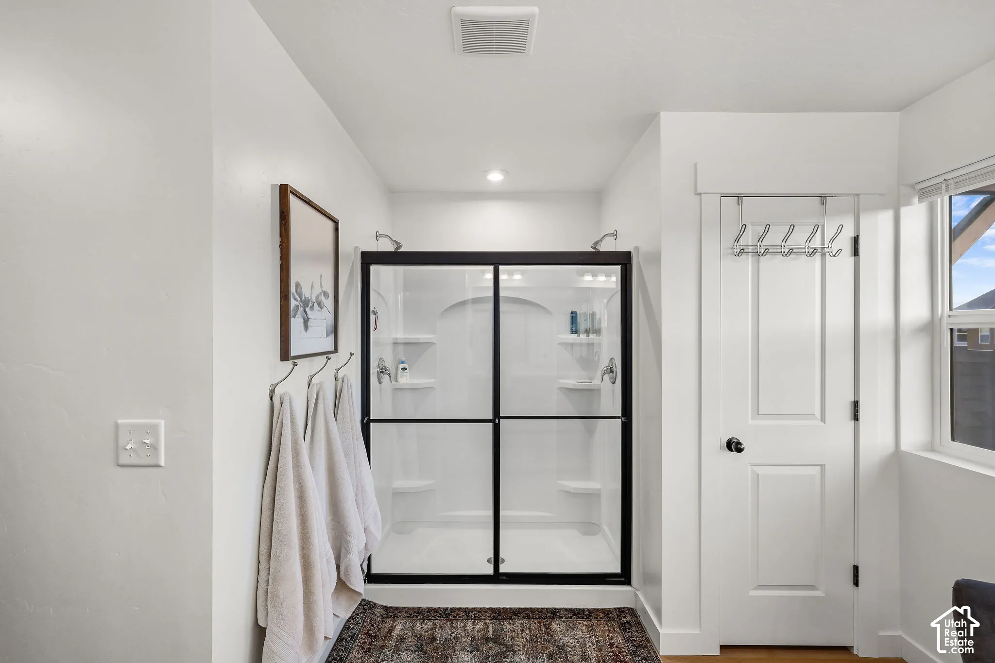 Walk-in shower featuring a white surround, integrated shelving, and a matte black frame, complemented by a white two-panel interior door with matte black hardware