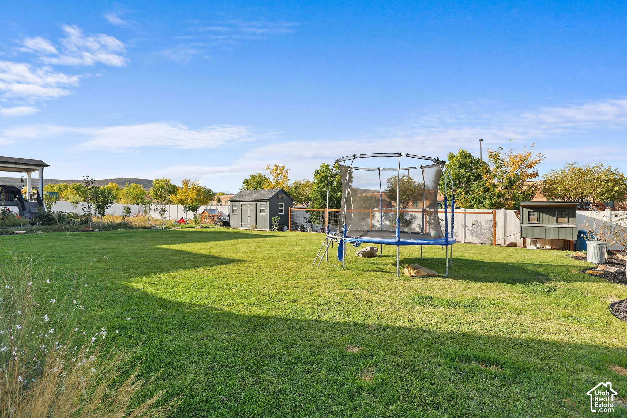 Expansive backyard featuring a level lawn, perimeter vinyl fencing, mature trees, and a detached storage shed