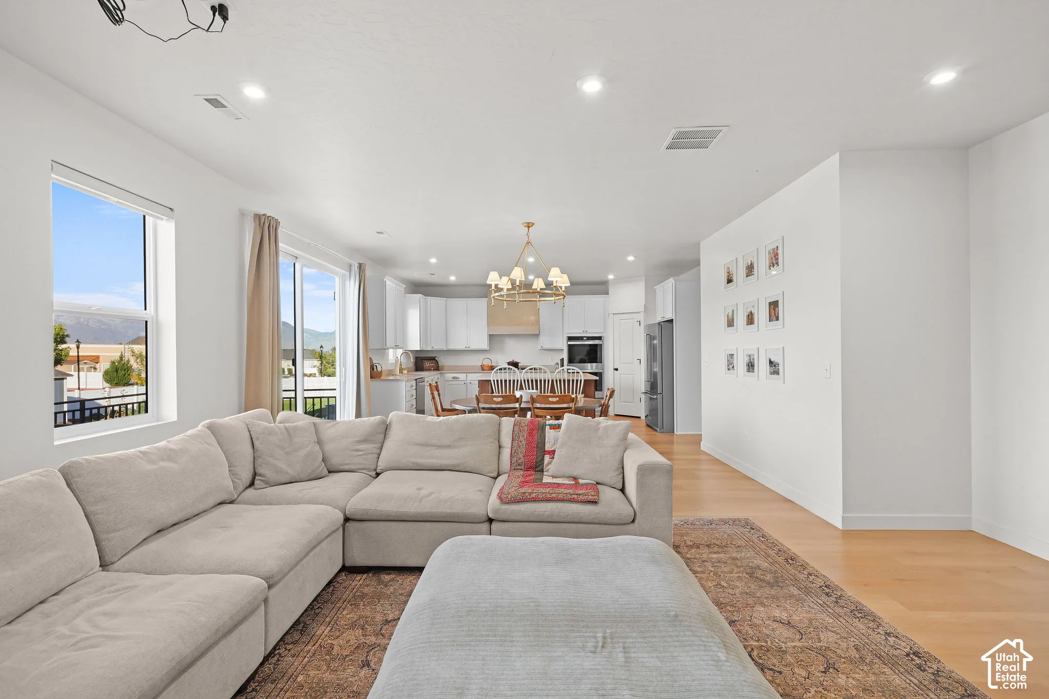 Open-concept interior featuring light wood-finish flooring, recessed lighting, a multi-tier chandelier, and a sliding glass door