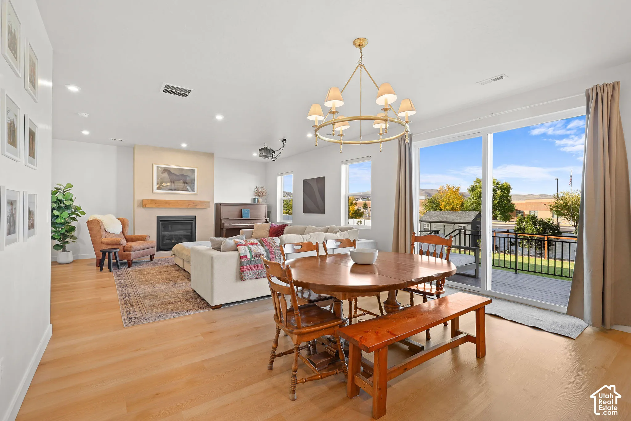 Open-concept interior featuring wood-finish flooring, a fireplace with a light-tone stone surround and wood mantel, a multi-arm chandelier, and large glass sliding doors