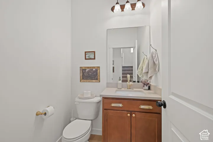 Wood-finish vanity with a rectangular sink, stone-composite countertop, metallic hardware, and wall-mounted three-light fixture