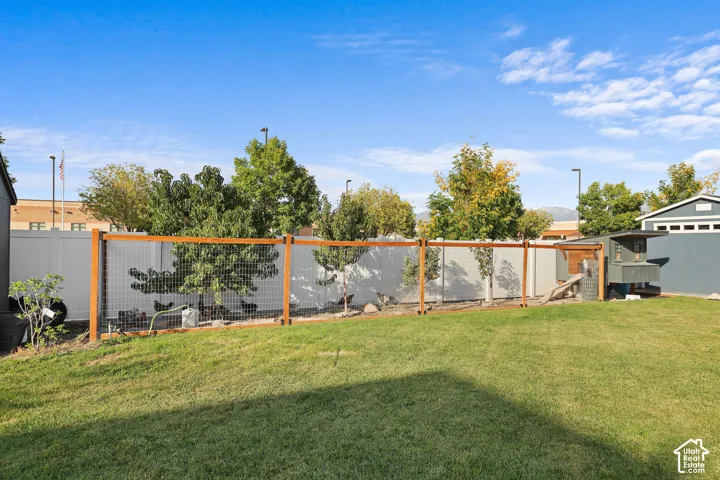 Expansive backyard featuring a manicured lawn, white vinyl perimeter fencing, integrated wood-framed wire enclosure, and a detached storage structure