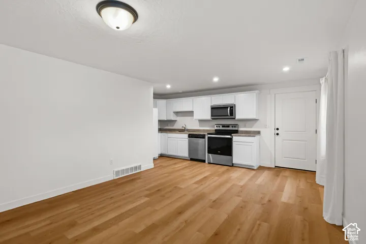 Kitchen featuring white cabinetry, stainless steel appliances, wood-finish flooring, and recessed lighting
