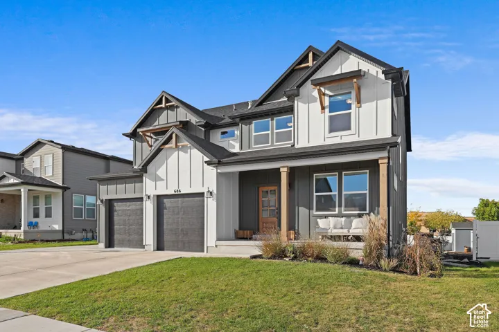 Two-story exterior featuring board-and-batten siding, dark-toned garage doors, decorative timber gable brackets, and a covered front porch with wood support columns