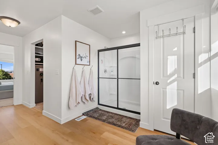 Walk-in shower featuring a glass enclosure with matte black framing, wood-finish flooring, and built-in closet shelving