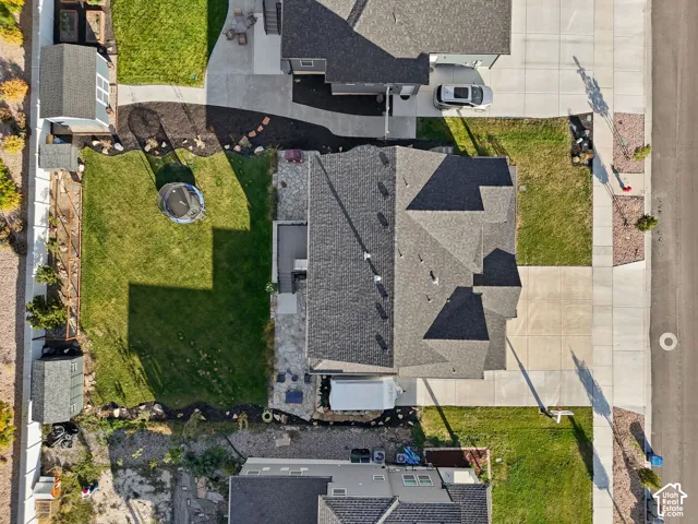 Aerial perspective of property featuring a multi-pitched asphalt shingle roof, concrete driveway, stone patio, fenced perimeter, and dedicated storage structure