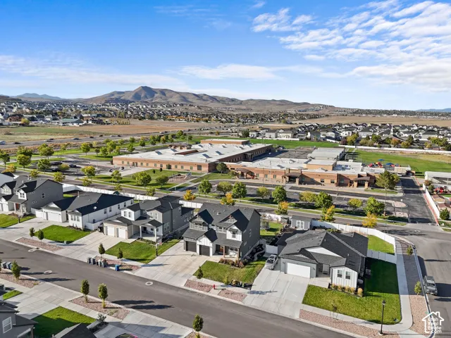 Aerial perspective of suburban residential neighborhood featuring paved street infrastructure, concrete driveways, manicured green spaces, and mountain terrain backdrop
