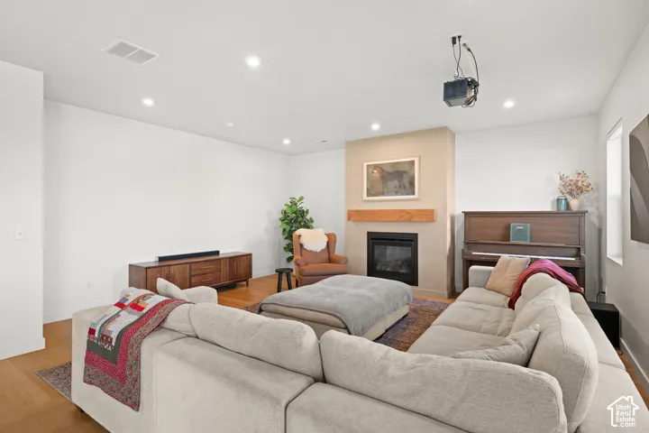 Living area featuring wood-finish flooring, recessed lighting, and a fireplace with a textured surround and natural wood mantel