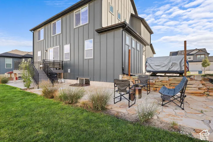 Vertical siding exterior featuring a raised deck with metal railings, flagstone patio, tiered natural stone retaining wall, and manicured lawn