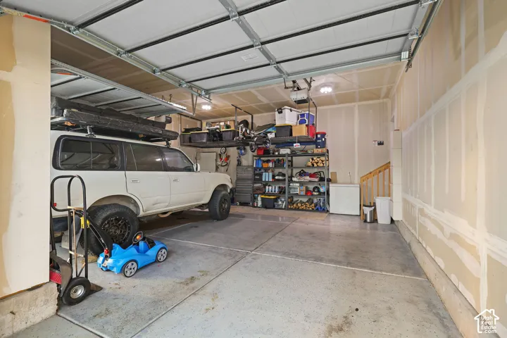 Attached multi-car garage featuring a concrete floor, sectional overhead door, ceiling-mounted storage racks, and unfinished drywall