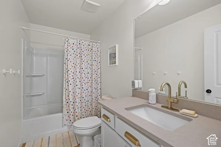 Bathroom featuring a vanity with a neutral-toned solid surface countertop, an undermount sink, and brass-finish hardware, paired with a white tub and shower combination with integrated shelving