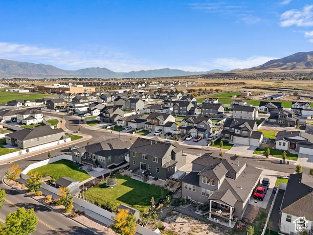 Aerial perspective featuring multi-story residential structures, fenced rear yards with manicured lawns, asphalt roadways, and mountainous topography