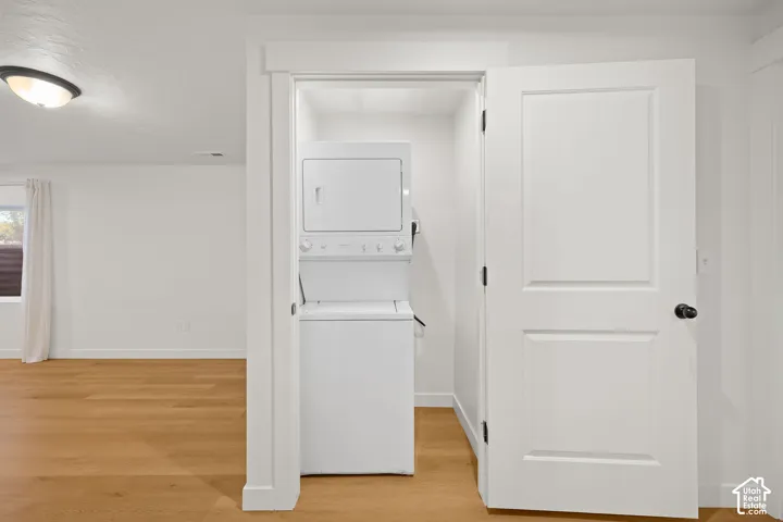 Dedicated laundry closet featuring a stackable washer and dryer, wood-finish flooring, and white interior trim