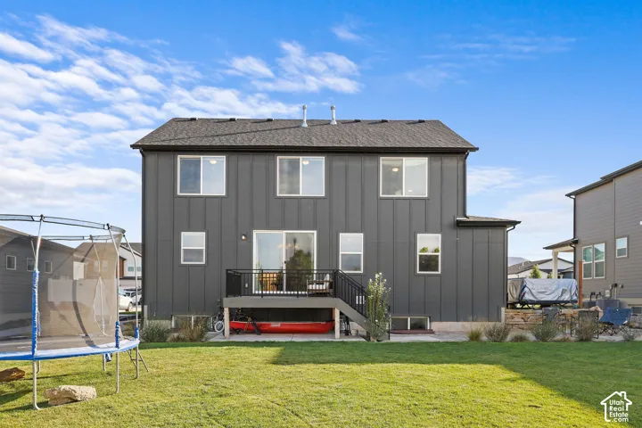 Two-story exterior featuring dark vertical siding, a raised deck with black metal railing, concrete patio, and a manicured lawn