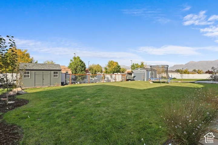 Expansive backyard featuring a level lawn, two detached storage structures, perimeter fencing, and a mountain backdrop