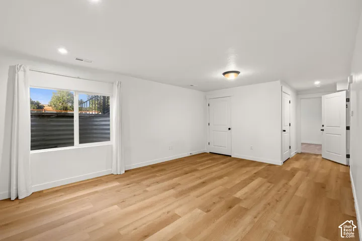 Neutral-toned room featuring wood-finish flooring, recessed lighting, and multiple interior doors with matte black hardware