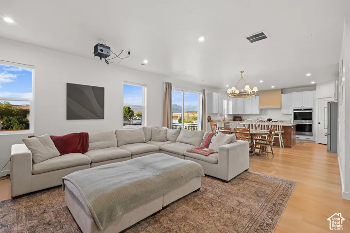 Open-concept interior featuring light wood-finish flooring, recessed lighting, double wall ovens, a custom range hood, and large windows with mountain scenery