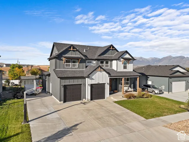 Two-story exterior featuring board-and-batten siding, dark-toned garage doors, decorative wood gable accents, a covered front porch with timber supports, and mountain scenery