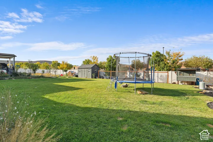 Expansive backyard featuring a level lawn, perimeter vinyl fencing, mature trees, and a detached storage shed