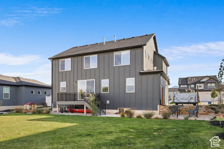 Two-story exterior featuring vertical metal siding, an elevated deck with black metal railings, a concrete patio, and stacked stone retaining wall