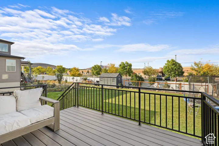 Elevated deck with composite wood-finish decking and black metal railing, overlooking a fenced backyard featuring a lawn and a detached storage shed