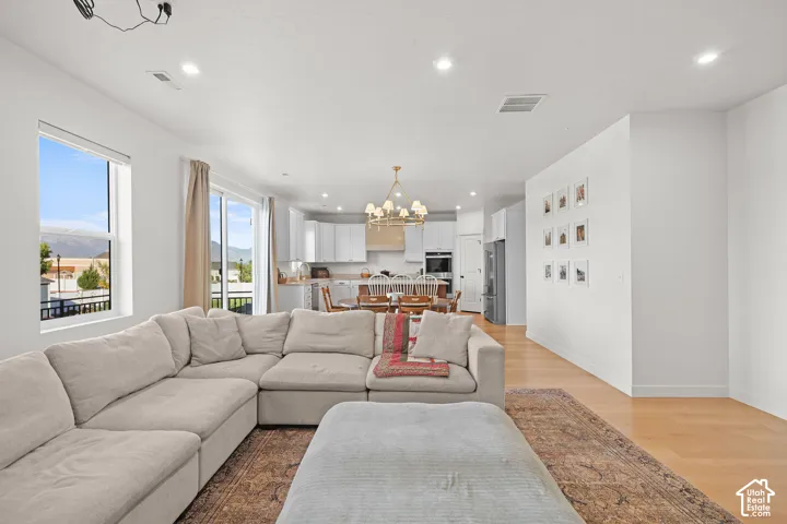 Open-concept interior featuring light wood-finish flooring, recessed lighting, a multi-tier chandelier, and a sliding glass door