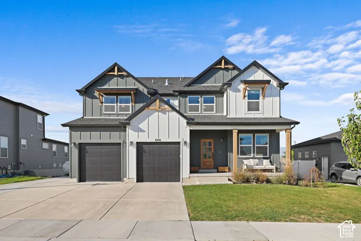 Two-story residence featuring vertical and horizontal siding, multi-gabled roofline, covered entryway with wood-finish supports, and an attached two-car garage