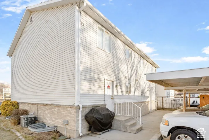 Two-story residence featuring light-toned horizontal siding, a stone veneer foundation, concrete exterior steps with a metal railing, and an attached covered carport