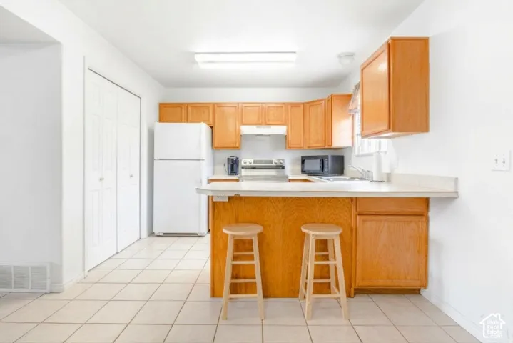 Kitchen featuring wood cabinetry, a breakfast bar, white appliances, and tile flooring