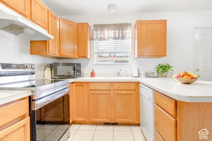 Kitchen featuring oak cabinetry, light-toned countertops, tile flooring, stainless steel range, and a dual-basin sink