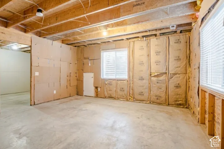 Unfinished interior space featuring exposed wood framing, concrete flooring, batt insulation, and dual windows with horizontal blinds