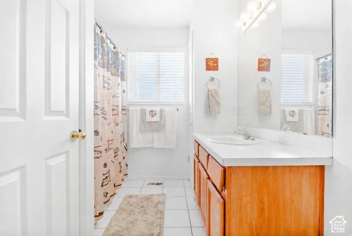 Bathroom featuring a white vanity with an integrated countertop sink, full-width wall mirror, wood-finish cabinetry, and ceramic tile flooring