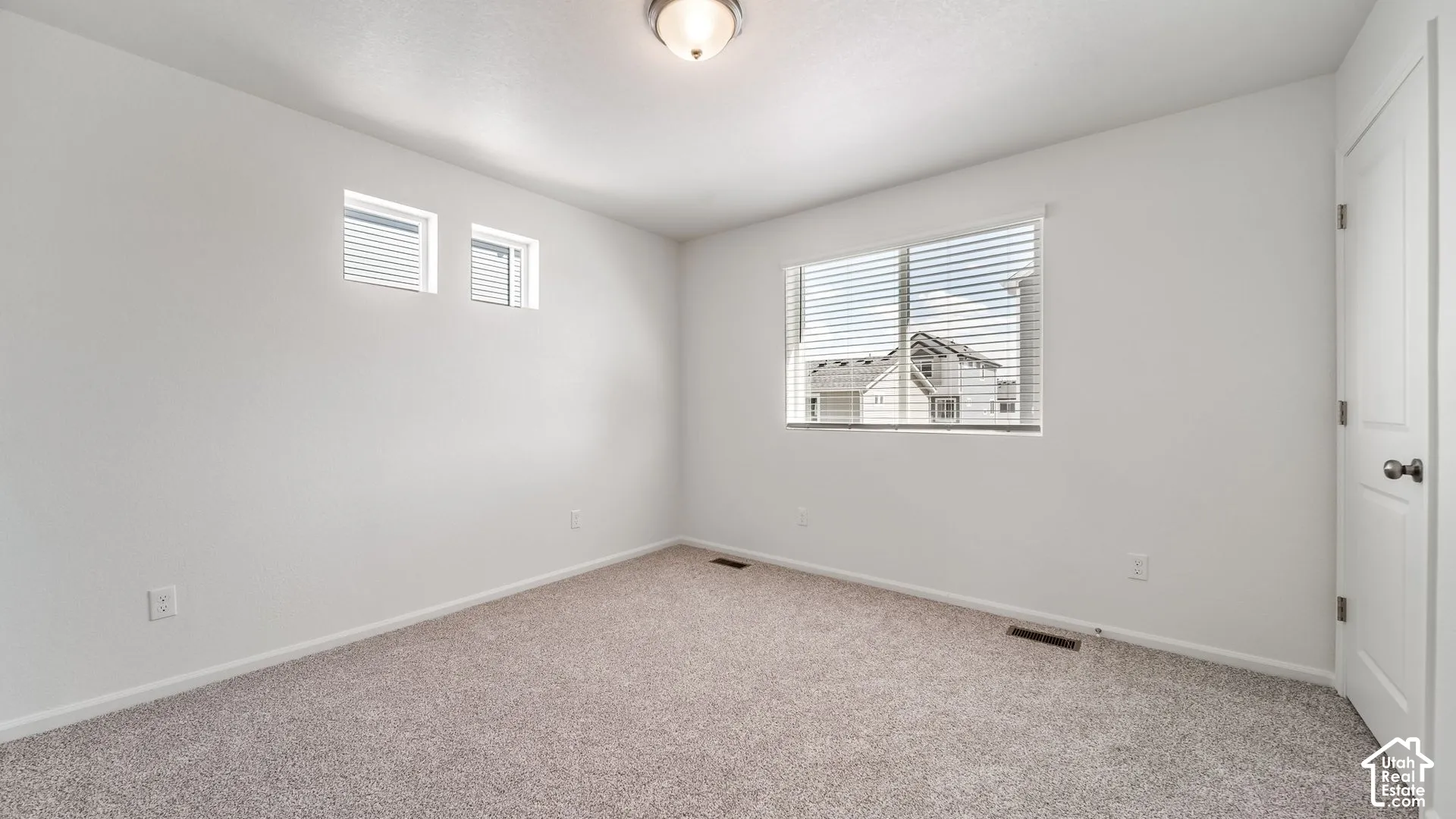 Neutral-toned wall-to-wall carpeting, high-reaching windows for natural illumination, overhead flush-mount lighting, and solid-core interior door with metallic hardware