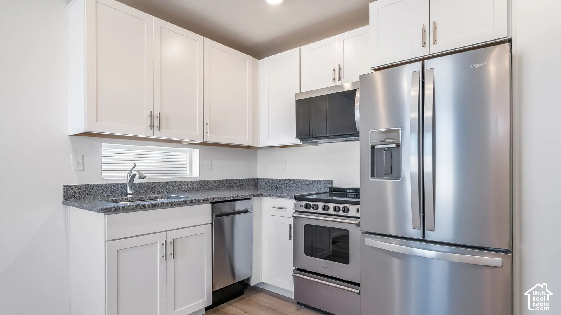 Kitchen featuring white shaker-style cabinetry, speckled stone-finish countertops, stainless steel appliances, and wood-finish flooring