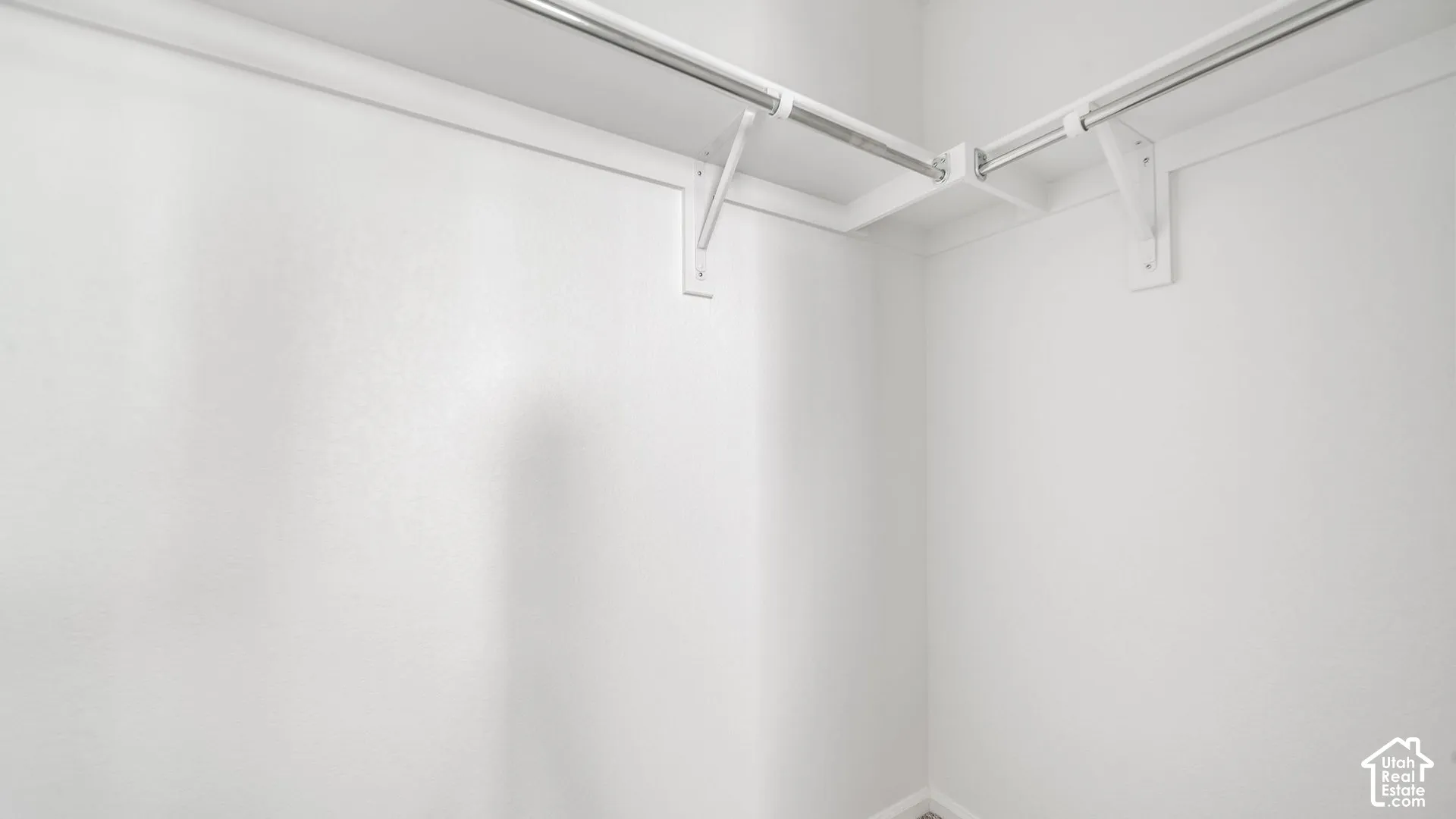 Walk-in closet featuring white-painted walls and dual-level metal clothes rods with integrated shelving