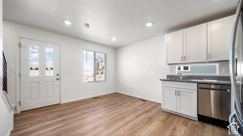 Kitchenette featuring white Shaker-style cabinetry, stone-finish countertops, stainless steel dishwasher, and wood-finish flooring