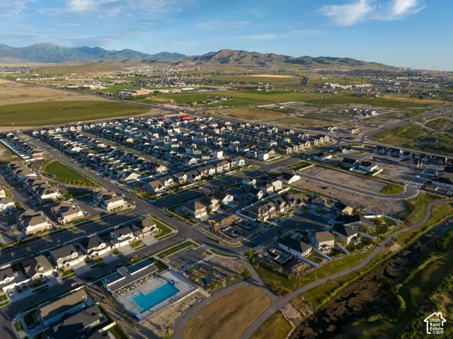 Aerial perspective of a suburban neighborhood featuring paved roadways, a community swimming pool, recreational space, and a mountainous backdrop