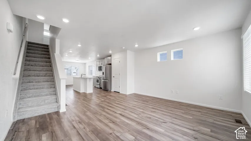 Open-concept interior featuring wood-finish flooring, recessed lighting, a staircase with carpeted treads, and a kitchen island with a stone-finish countertop