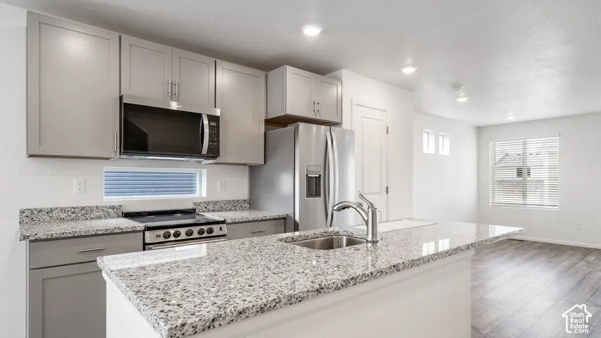 Kitchen featuring shaker-style cabinetry, stone-patterned countertops, a central island with an undermount sink, stainless steel appliances, and wood-finish flooring