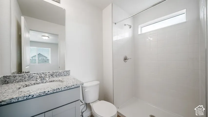 Bathroom featuring a light-toned vanity with a stone-composite countertop, undermount sink, ceramic tile shower surround, and horizontal transom window