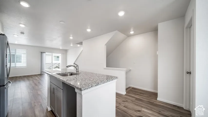 Kitchen island with stone-surface countertop, stainless steel undermount sink, integrated cabinetry, wood-finish flooring, and recessed ceiling lighting