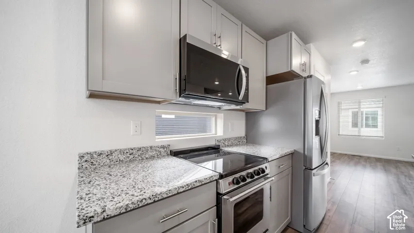 Kitchen featuring grey shaker-style cabinetry, stone-finish countertops, stainless steel appliances, and wood-finish flooring