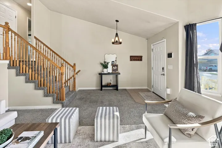 Vaulted ceilings, staircase with wood handrails and balusters, tile entryway flooring, carpeted flooring, and pendant lighting