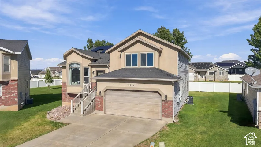 Two-story exterior featuring a mix of stucco and brick siding, an attached two-car garage, roof-mounted solar panels, and a concrete driveway