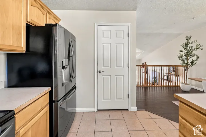Kitchen area featuring light-finish cabinetry, tile flooring, and a black refrigerator