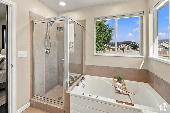 Glass-enclosed shower with tiled surround, deep soaking tub, and windows providing natural light